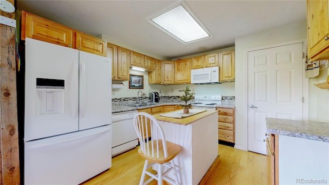 kitchen with light hardwood / wood-style floors, white appliances, a kitchen island, a kitchen breakfast bar, and sink