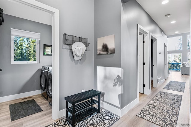 hall with light wood-type flooring, separate washer and dryer, and a wealth of natural light