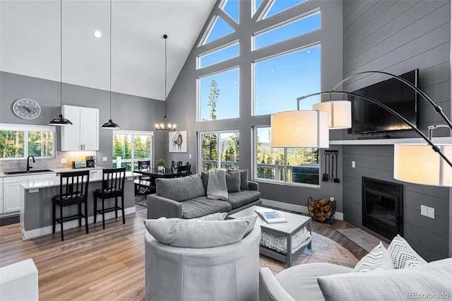 living room featuring a large fireplace, light hardwood / wood-style floors, high vaulted ceiling, and sink