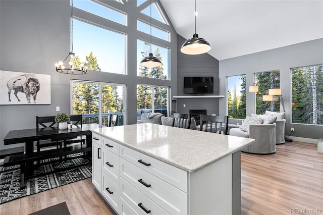 kitchen featuring a large fireplace, light hardwood / wood-style flooring, high vaulted ceiling, white cabinets, and hanging light fixtures