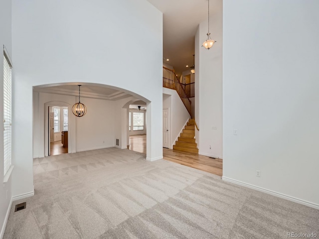 7447 Soapstone Way, Castle Rock, CO 80108 - unfurnished living room featuring arched walkways, a towering ceiling, carpet, plenty of natural light, and stairs