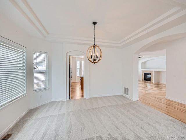 carpeted spare room featuring a chandelier, a tile fireplace, and a raised ceiling