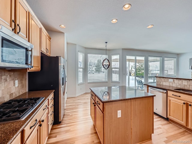 kitchen with a center island, stainless steel appliances, backsplash, decorative light fixtures, and light hardwood / wood-style flooring