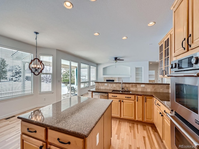 kitchen with stainless steel appliances, decorative light fixtures, light brown cabinets, sink, and light hardwood / wood-style floors