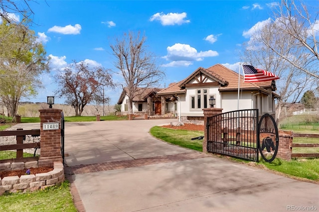 view of front of property featuring curved driveway, a tiled roof, stucco siding, fence, and a gate
