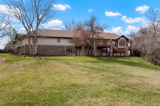 rear view of house featuring stucco siding, stone siding, stairs, a tiled roof, and a lawn