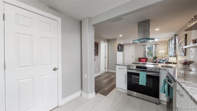 kitchen featuring electric stove, island range hood, white cabinets, a peninsula, and light stone countertops