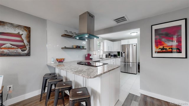 kitchen featuring sink, island exhaust hood, white cabinetry, stainless steel appliances, and a breakfast bar area