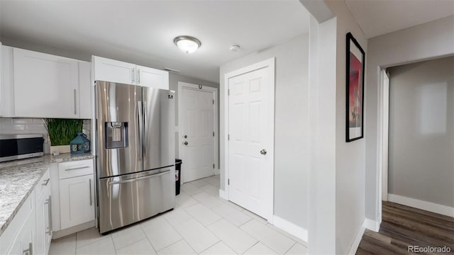 kitchen featuring baseboards, white cabinetry, backsplash, light stone countertops, and appliances with stainless steel finishes