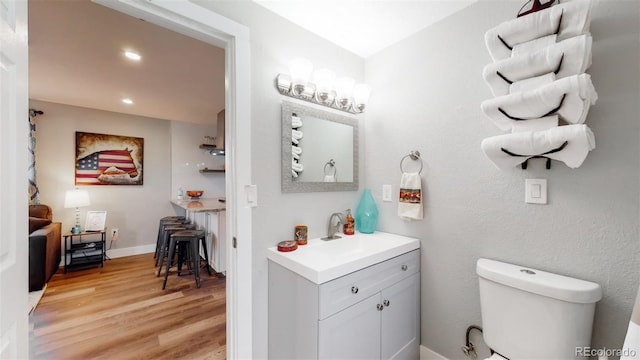 half bath with wood finished floors, recessed lighting, vanity, and toilet