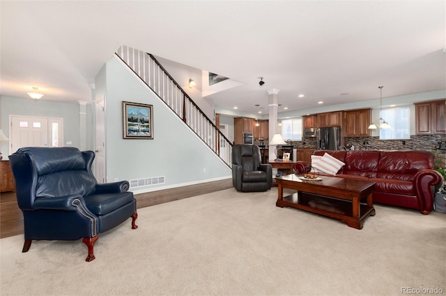 living room with stairway, light colored carpet, visible vents, and ornate columns