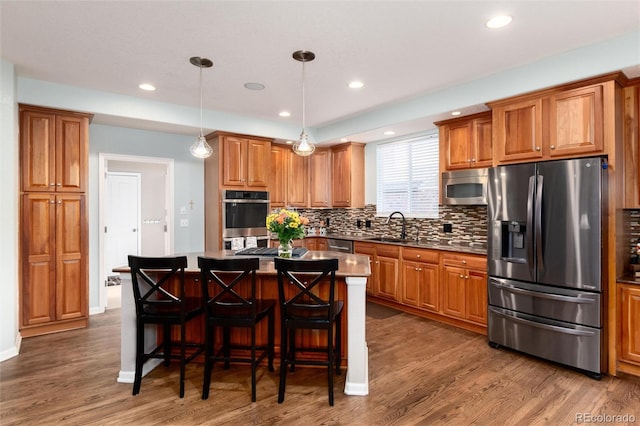 kitchen with stainless steel appliances, brown cabinets, a sink, and wood finished floors