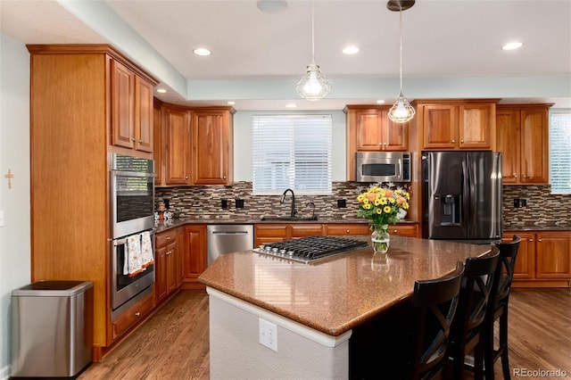 kitchen featuring a center island, decorative light fixtures, stainless steel appliances, light wood-type flooring, and sink