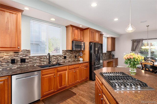 kitchen with pendant lighting, stainless steel appliances, a notable chandelier, dark stone counters, and sink