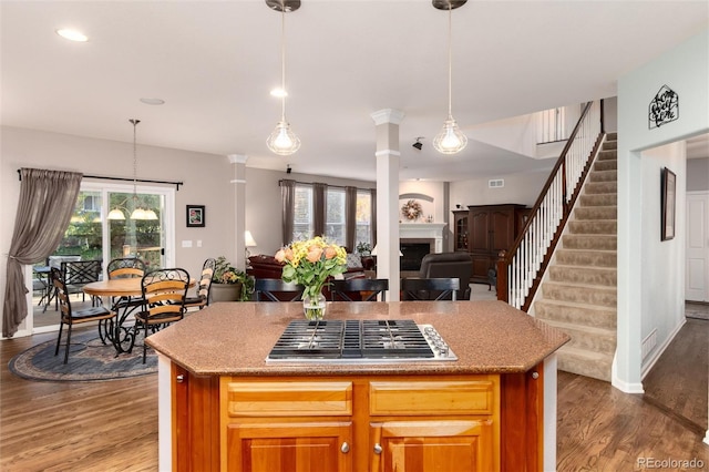 kitchen with decorative columns, stainless steel gas stovetop, a fireplace, and wood finished floors