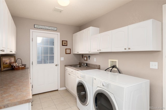 clothes washing area with sink, washing machine and clothes dryer, light tile patterned floors, and cabinets