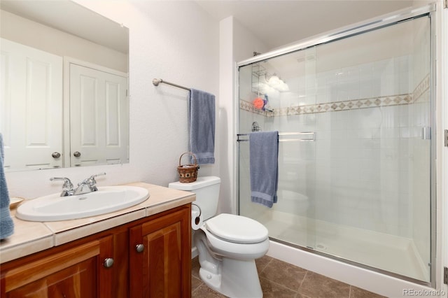 bathroom featuring toilet, vanity, a shower with shower door, and tile patterned floors