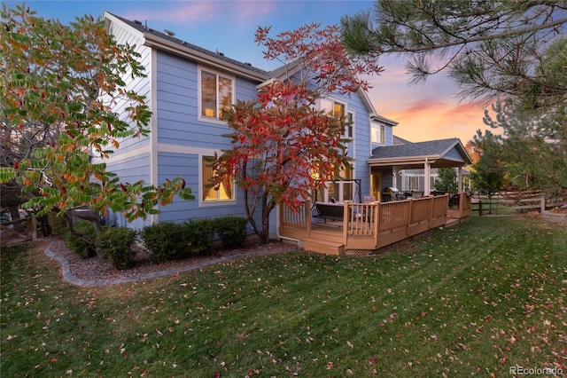 back house at dusk with a yard and a wooden deck