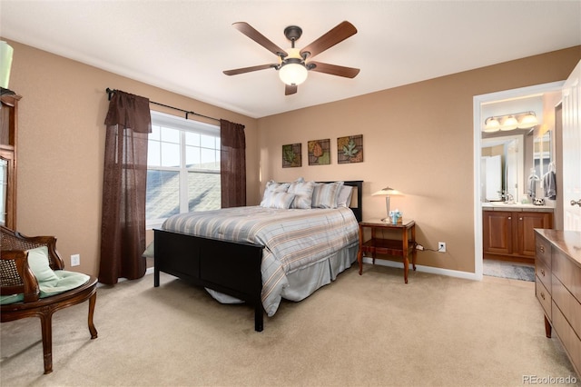 bedroom featuring light colored carpet, ceiling fan, baseboards, and ensuite bathroom