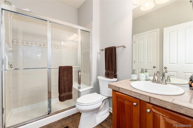 bathroom featuring wood finished floors, a shower stall, toilet, and vanity