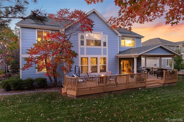 back of house featuring a deck, a shingled roof, and a lawn