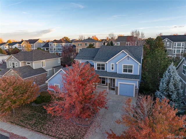 traditional-style home featuring an attached garage, driveway, stone siding, roof with shingles, and a residential view