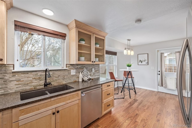 kitchen with tasteful backsplash, light brown cabinets, appliances with stainless steel finishes, light wood finished floors, and a sink