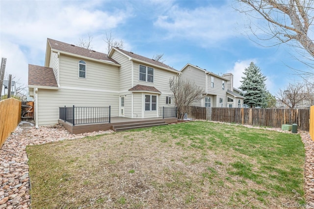 back of property with a shingled roof, a fenced backyard, a wooden deck, and a lawn