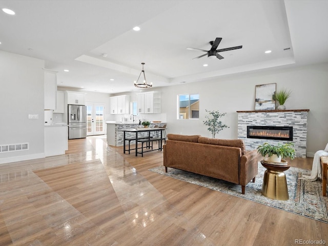 living room featuring visible vents, a glass covered fireplace, a tray ceiling, and light wood finished floors