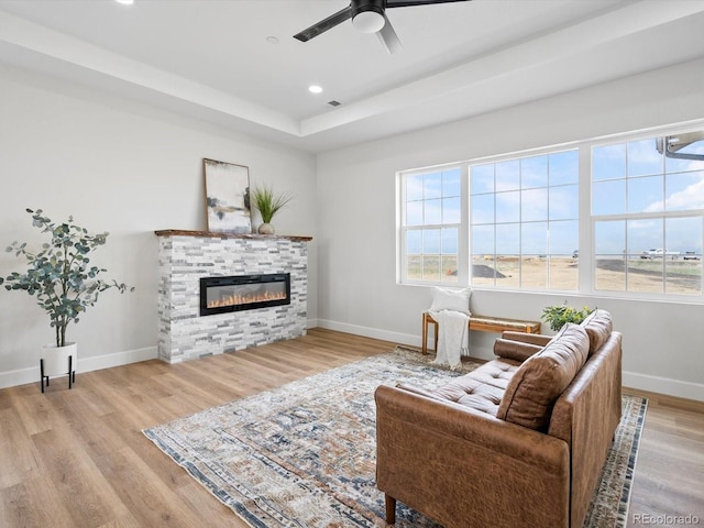 living room with baseboards, light wood-style flooring, a glass covered fireplace, and a raised ceiling