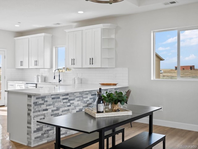 kitchen with white cabinets, backsplash, light countertops, a sink, and light wood-style flooring