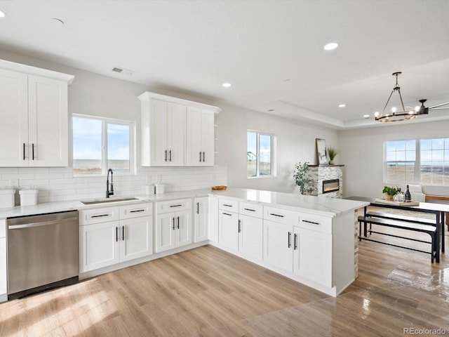 kitchen featuring dishwasher, a sink, light wood-style floors, a peninsula, and tasteful backsplash