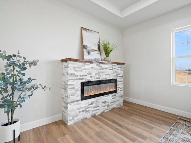 unfurnished living room with baseboards, wood finished floors, and a stone fireplace