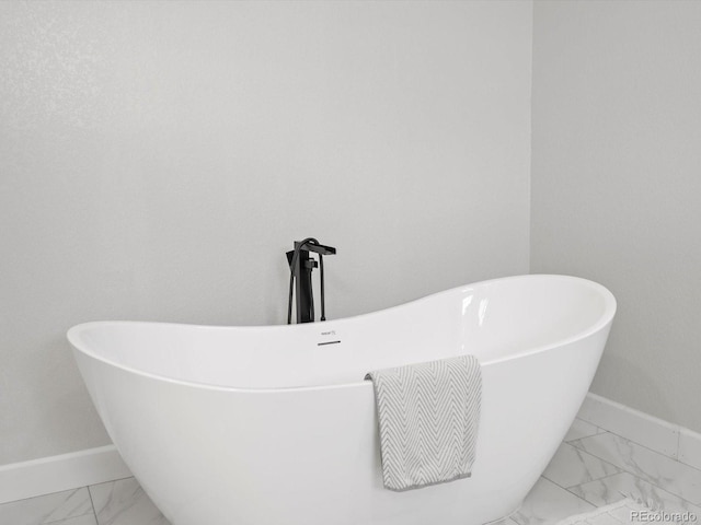 full bath with a freestanding tub, marble finish floor, and baseboards