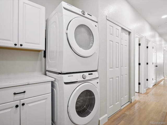 laundry room with cabinet space, light wood finished floors, and stacked washer / dryer