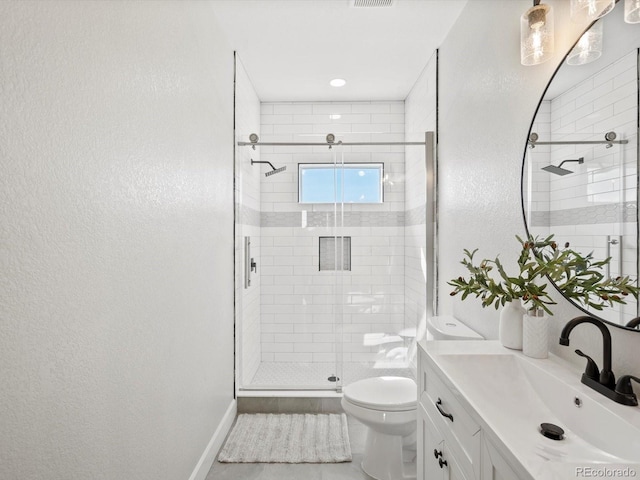 full bath featuring a stall shower, toilet, baseboards, a textured wall, and vanity