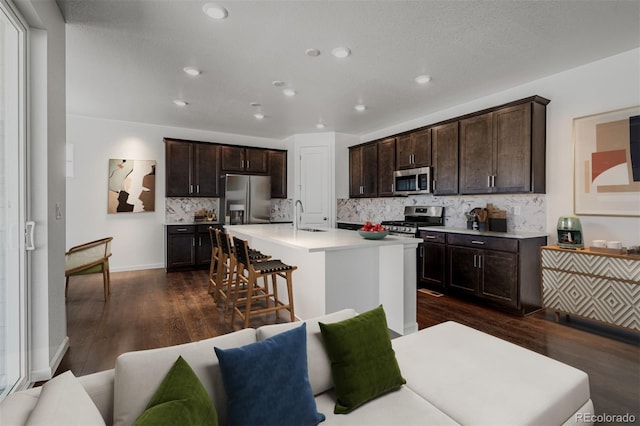 kitchen featuring dark hardwood / wood-style flooring, dark brown cabinets, stainless steel appliances, sink, and a center island with sink