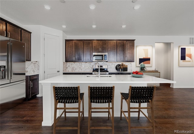 kitchen with sink, decorative backsplash, an island with sink, dark brown cabinets, and stainless steel appliances