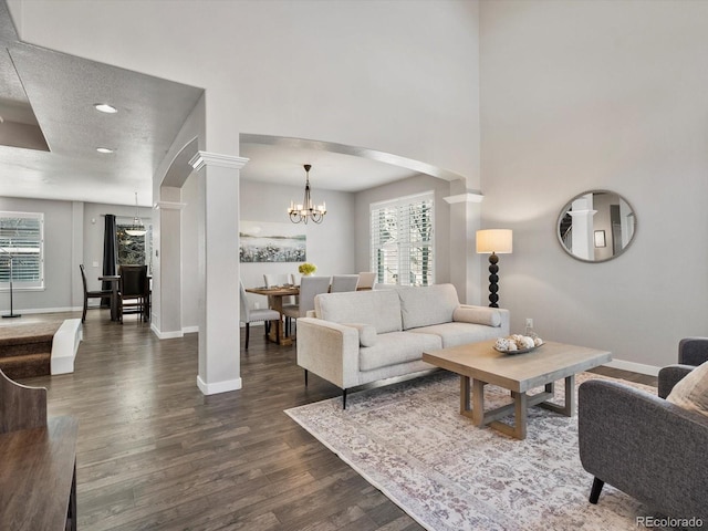 living room with an inviting chandelier, dark hardwood / wood-style flooring, and ornate columns