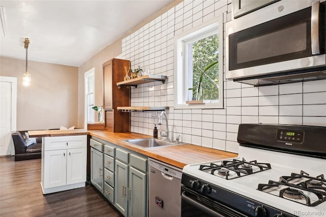 kitchen with sink, butcher block countertops, decorative light fixtures, kitchen peninsula, and stainless steel appliances