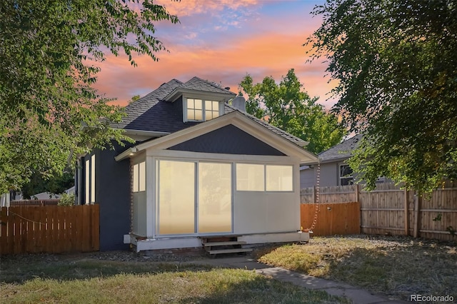 back house at dusk featuring a lawn