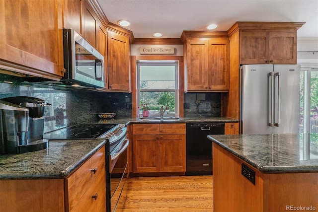 kitchen featuring stainless steel appliances, a sink, light wood-style floors, brown cabinets, and dark stone countertops