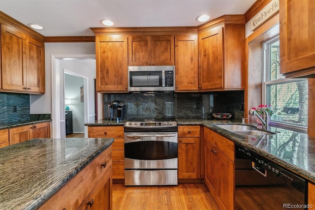 kitchen with appliances with stainless steel finishes, a sink, dark stone counters, light wood-type flooring, and brown cabinets