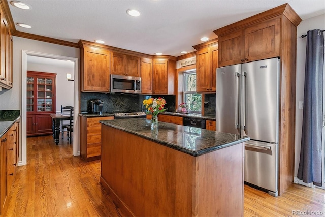 kitchen featuring appliances with stainless steel finishes, light wood-style floors, decorative backsplash, dark stone countertops, and a kitchen island