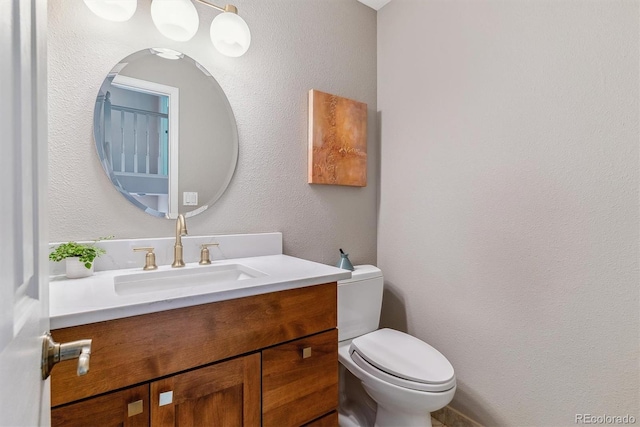 half bathroom with toilet, vanity, and a textured wall