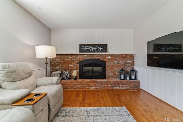 living room with wood finished floors, a wainscoted wall, and a brick fireplace
