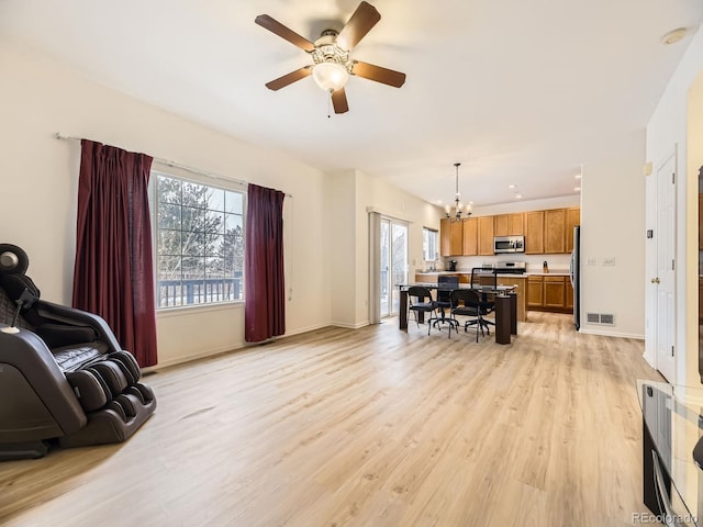 living room featuring ceiling fan with notable chandelier and light hardwood / wood-style flooring