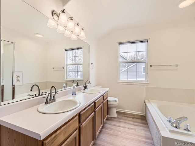 bathroom featuring lofted ceiling, tiled tub, toilet, wood-type flooring, and vanity