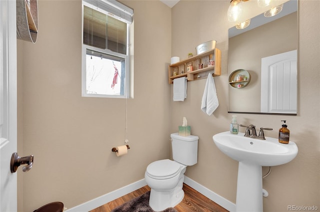 half bathroom featuring a sink, toilet, wood finished floors, and baseboards