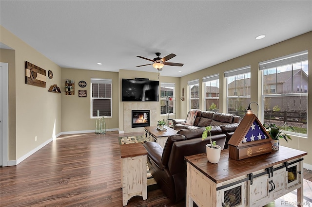living room with dark wood-type flooring, a tile fireplace, baseboards, and ceiling fan